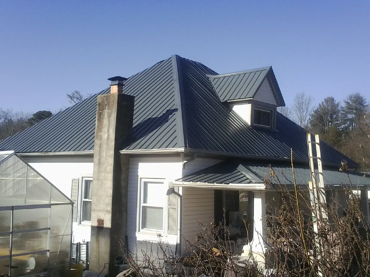 Dark blue standing seam metal roof on a white farmhouse with dormer — Slate & Tile Roof Repair by Roofing Brothers in Montclair