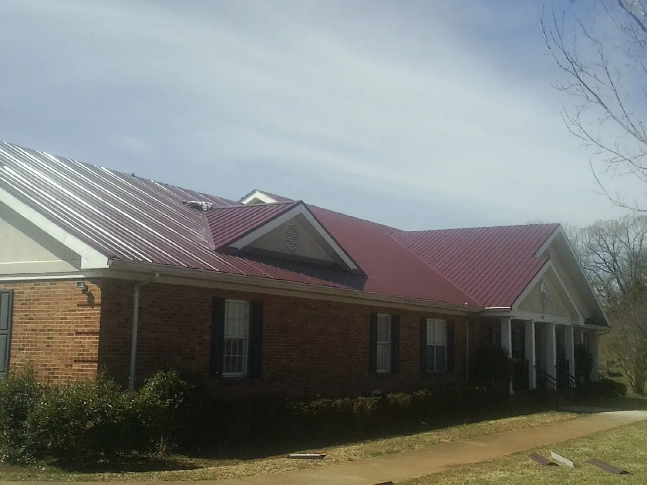 Red metal roof with gabled entries on a long brick building, from a Hail Damage Roof Repair job in Montclair