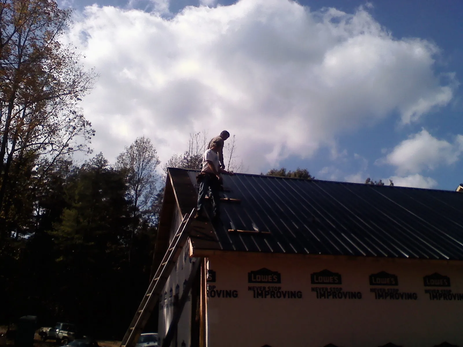 Roofer fastening dark metal panels high against a cloudy sky, from a Roof Inspection job in Montclair
